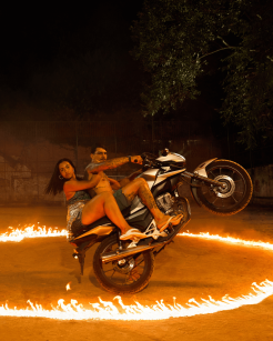 Casal empinando moto atravessa círculo em chamas durante gravação da campanha de verão 2025 da Rabanne no Rio de Janeiro; cena destaca a estética do funk carioca, com elementos de dança, estilo periférico e expressão urbana.